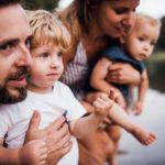 A young family with two toddler children outdoors by the river in summer.