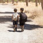 multiethnic latin and caucasian children walking together on the woods with backpacks on summercamp